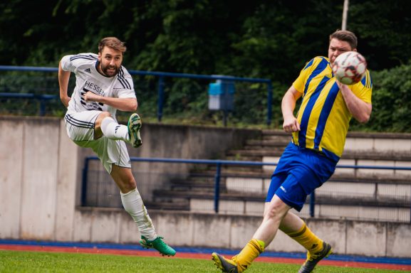Zwei Fußballspieler im Wettkampf, einer schießt, der andere versucht zu blocken.