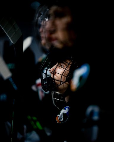 Ein junger Eishockeyspieler mit Helm und Gittermaske, intensiv in Gedanken.