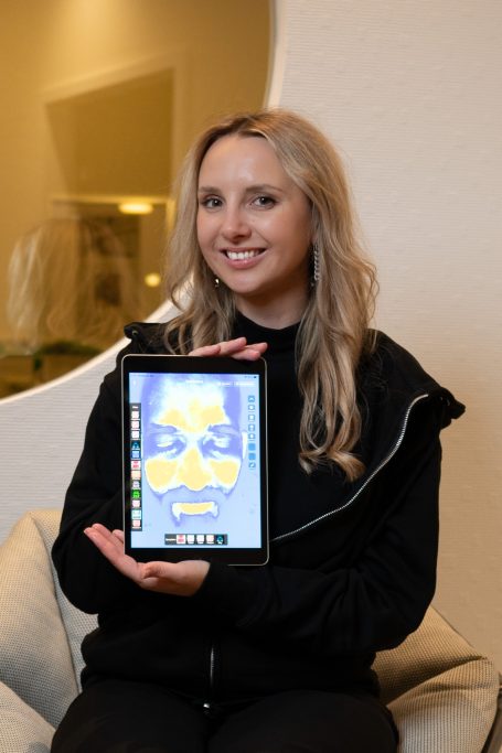 Eine lächelnde Frau hält ein Tablet mit einer bunten Anzeige in der Hand.