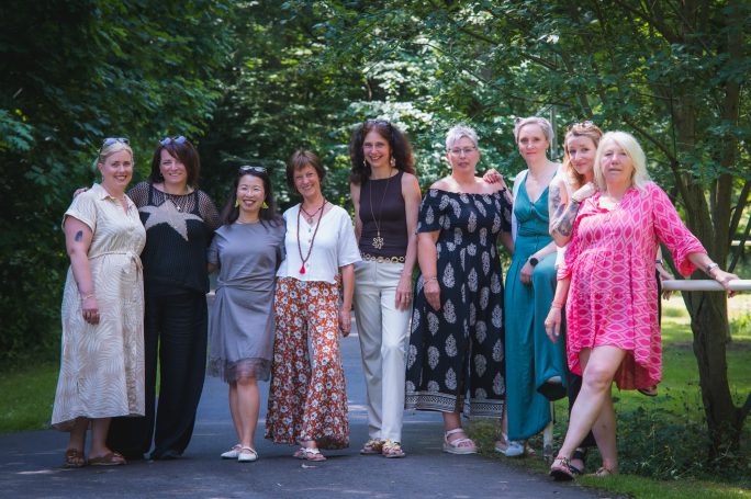 Eine Gruppe von neun Frauen steht in einem Park, umgeben von Bäumen.