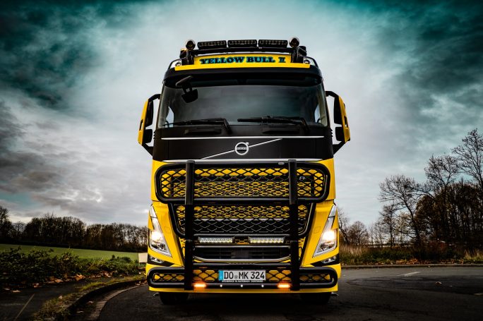 Gelber Lkw mit prominentem Kühlergrill unter bewölktem Himmel.