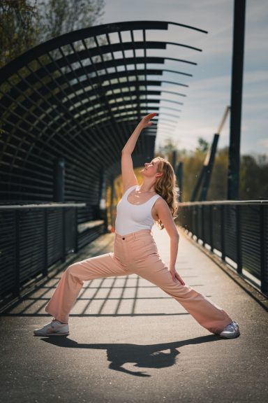 Eine Frau in sportlicher Pose auf einer Brücke, umgeben von natürlichem Licht.
