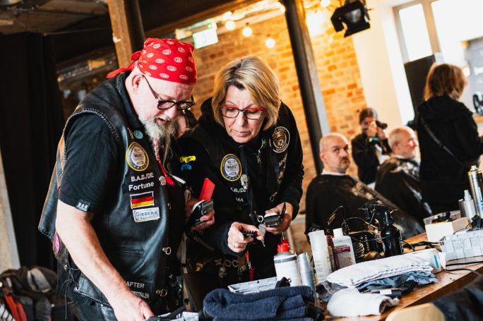 Zwei Personen in Ausrüstung betrachten gemeinsam ein Smartphone bei einer Veranstaltung.