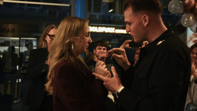 Ein Mann spricht mit einer Frau in einem festlichen, belebten Umfeld.