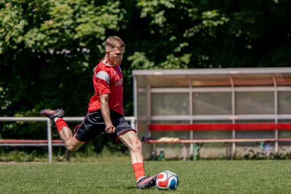 Junger Sportler tritt einen Fußball auf einem Trainingsplatz.