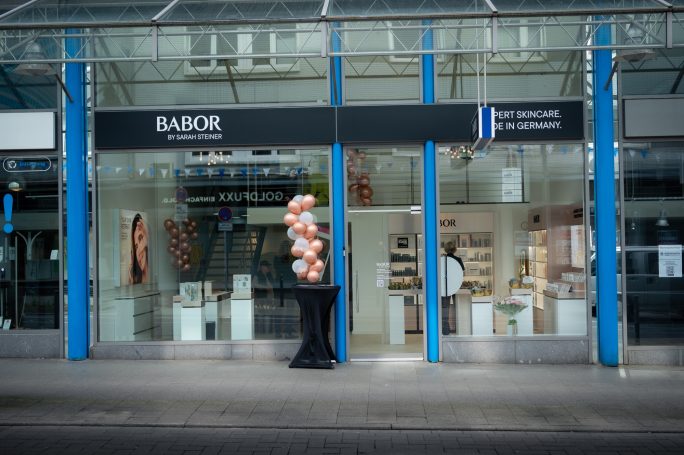 Moderne Ladenfront mit großen Fenstern und einer eleganten Blumendekoration.