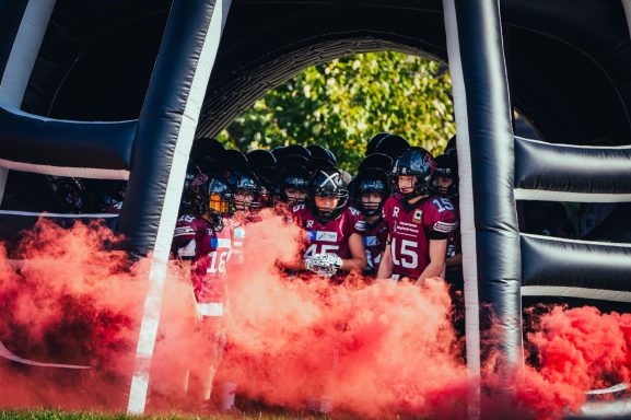 Footballmannschaft, die durch einen aufblasbaren Bogen mit rotem Rauch eintritt.