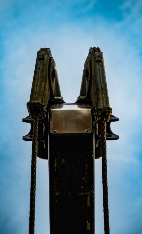 Ansicht einer robusten Kranspitze vor blauem Himmel, mit Seilen, die nach unten führen.