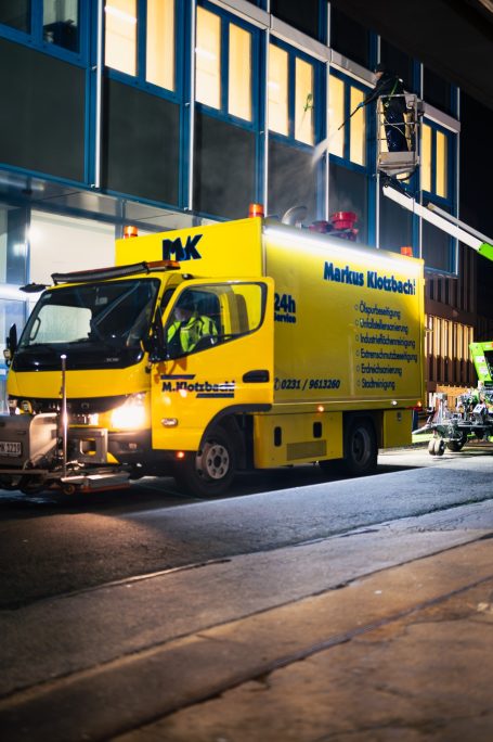 Gelber Kastenwagen parkt vor einem Gebäude, mit einem Arbeitskorb für Höhenarbeiten.