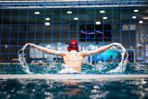 Person beim Schwimmen in einem Pool, Wasser spritzt umher, Fokus auf Rückenansicht.