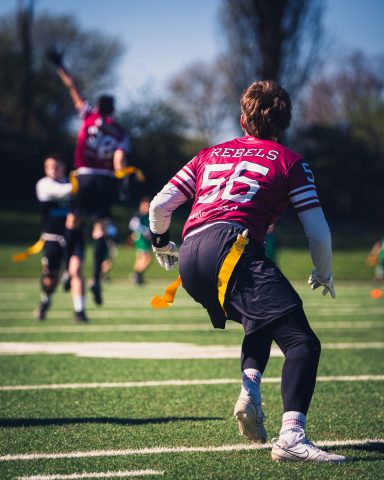 Ein Spieler wirft den Ball während eines Flagfootball-Spiels, im Hintergrund orange Fähnchen.