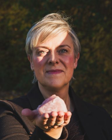 Frau mit kurzen blonden Haaren hält einen klaren Kristall in der Hand.