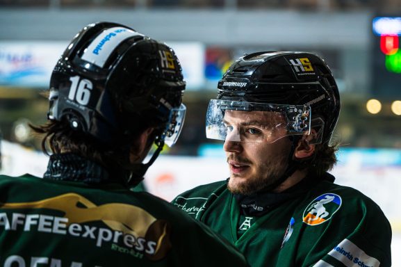 Zwei Eishockeyspieler in grünen Trikots Gespräche auf dem Eis.