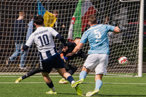 Zwei Fußballspieler im Wettkampf, während der Torwart einen Schuss abwehrt.