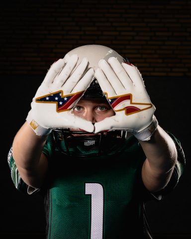 Ein junger Footballspieler zeigt mit Händen ein Handzeichen und trägt einen Helm.