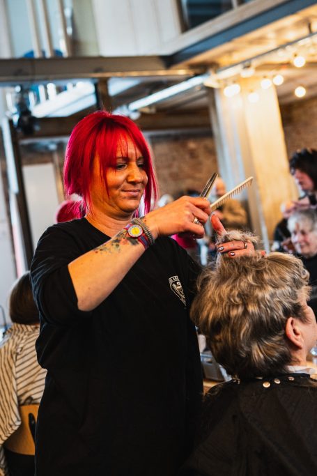 Friseurin mit roten Haaren schneidet Haare eines Kunden in einem modernen Salon.