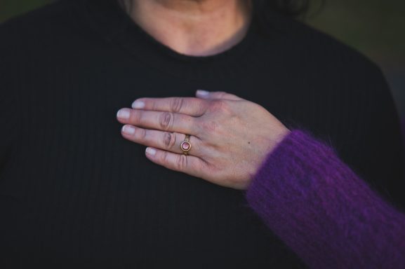 Eine Hand liegt sanft auf der Brust einer Person mit einem Ring.