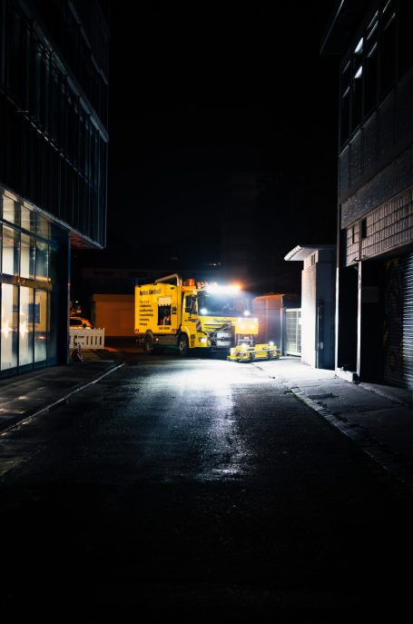 Arbeitsmaschine bei Nacht, beleuchtet durch Scheinwerfer in einer engen Gasse.