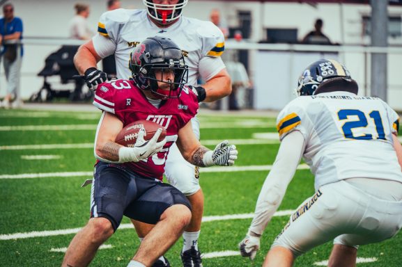 Footballspiel: Spieler im roten Trikot mit dem Ball wird von einem Gegner in Blau angegriffen.