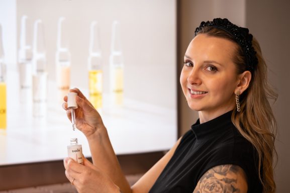 Frau mit langen Haaren hält eine Pipette vor einer Reihe von Fläschchen.