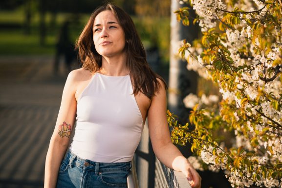 Junge Frau in einem weißen Top steht neben blühenden Bäumen im Freien.