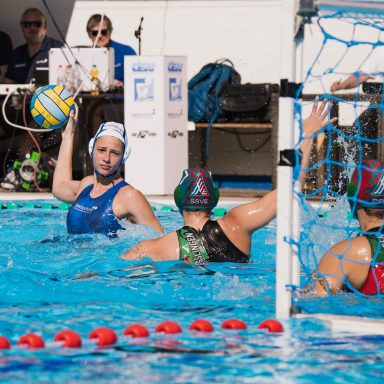 Wasserballspiel mit Spielerinnen im Wasser und einem Tor im Hintergrund.