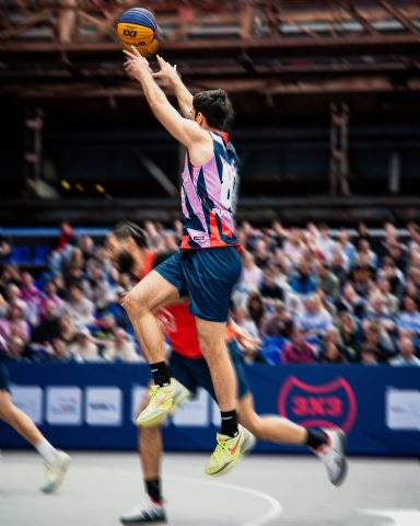Spieler springt, um einen Basketballkorb zu treffen, während ein Gegner ihn verteidigt.