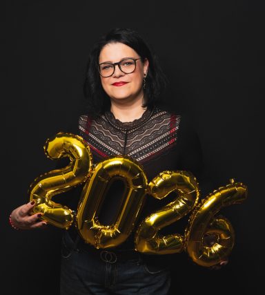Eine Person mit Brille hält goldene Luftballons, die "2026" zeigen.