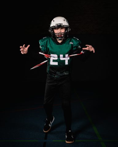 Junge in Football-Ausrüstung mit der Nummer 24, posiert auf dunklem Hintergrund.