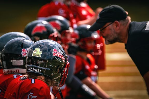 Trainer spricht mit jungen Footballspielern in roten Uniformen auf dem Feld.
