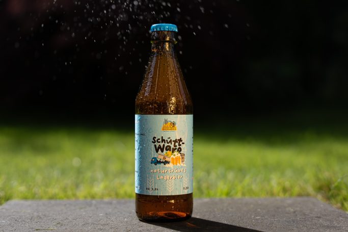 Flasche mit Erfrischungsgetränk, orangefarbenes Etikett, auf grünem Rasen.