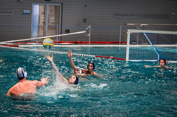 Wasserballspiel mit Spielern, die um den Ball im Wasser kämpfen.