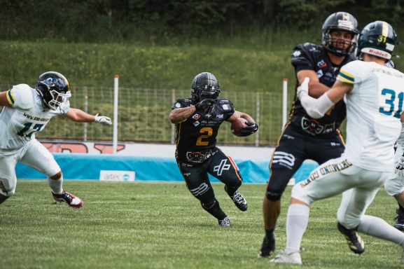 Ein Footballspieler verläuft zwischen zwei Verteidigern auf dem Feld.