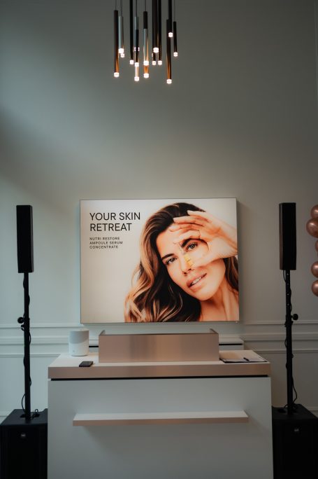 Helle Räume mit einer Frau, die ihre Hand am Gesicht hält und werbendes Display im Hintergrund.