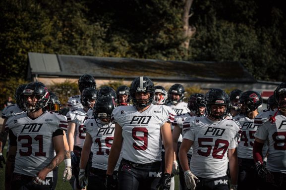 Gruppierung von American-Football-Spielern in weißen Trikots, auf einem Spielfeld.