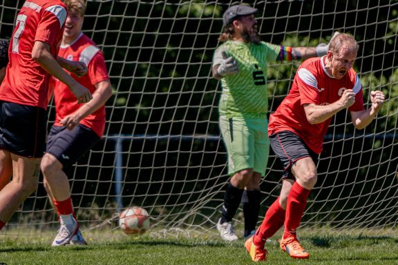 Fußballspiel: Spieler jubeln nach einem Tor, Torwart beobachtet gespannt.
