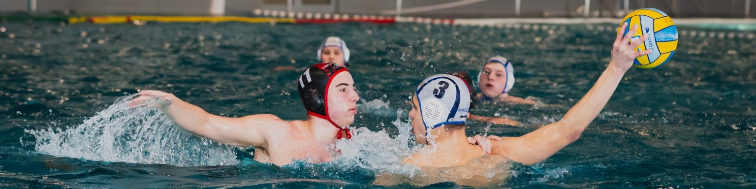 Wasserspieler in Aktion, einer hebt den Ball zum Wurf, umgeben von Mitspielern.