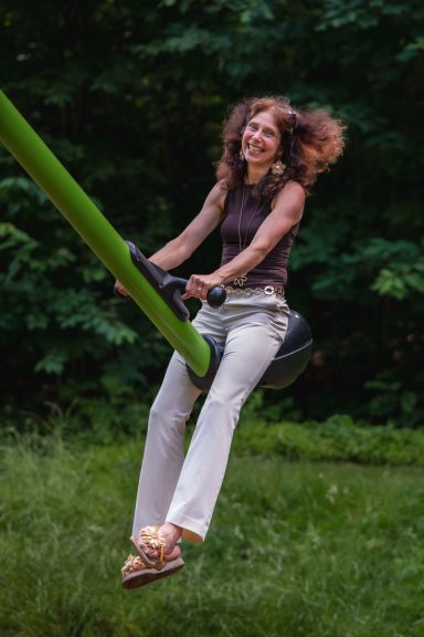 Eine lächelnde Frau schwingt auf einer grünen Schaukel in einem Park.