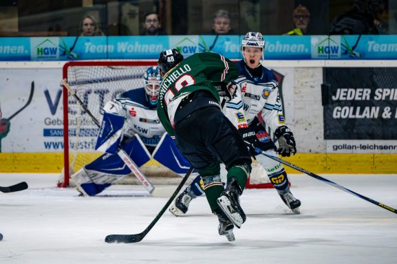 Eishockeyspieler schießt den Puck auf das Tor, ein Torwart ist bereit.