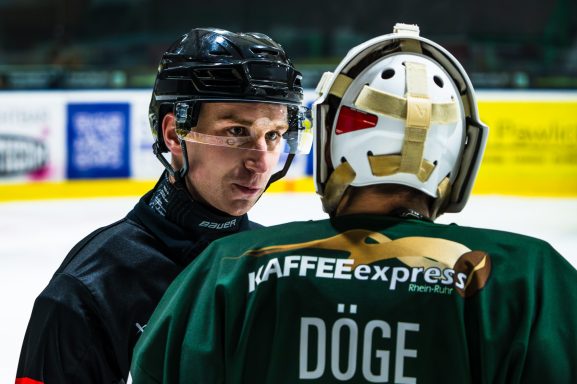 Trainer spricht mit Spieler in Eishockey-Rüstung auf dem Eisfeld.