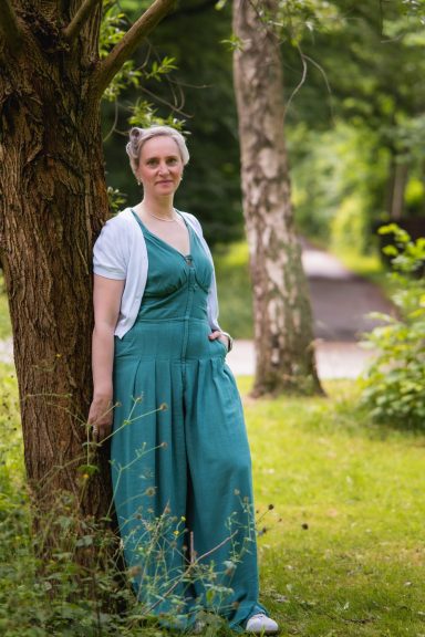 Eine Frau in einem grünen Overall steht an einem Baum in einem Garten.