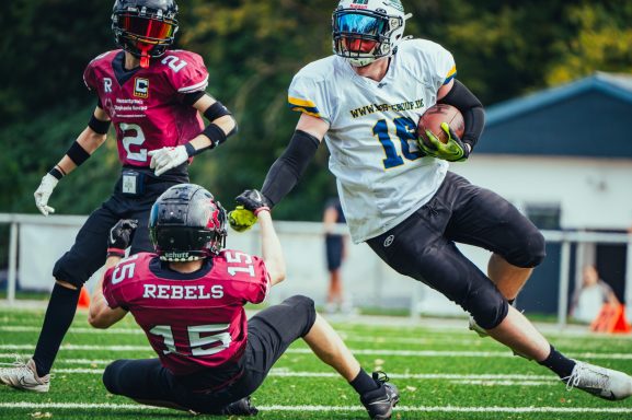 Ein Footballspieler in Weiß weicht einem tacklenden Gegner in Rot aus.