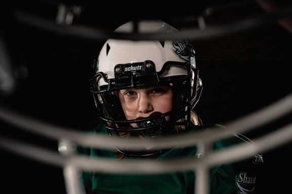 Ein sportlich gekleideter Spieler mit Helm schaut konzentriert durch ein Gitter.