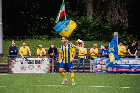 Fußballspieler feiert mit Fahnen in einer jubelnden Menge im Hintergrund.