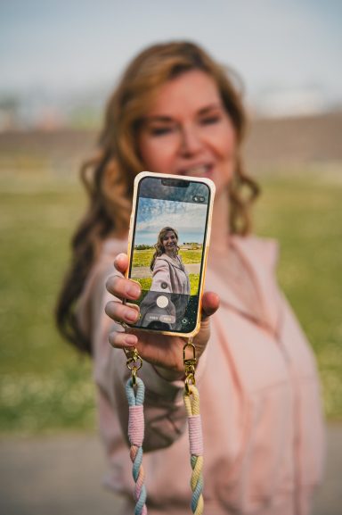 Frau präsentiert ein Smartphone mit einem Foto einer Landschaft auf dem Bildschirm.