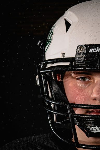 Junger Fußballspieler in schwarzer Uniform mit weißem Helm, nur die Hälfte des Gesichts sichtbar.