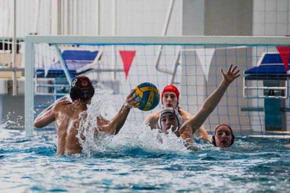 Wasserballspiel mit vier Spielern im Wasser und einem Ball.