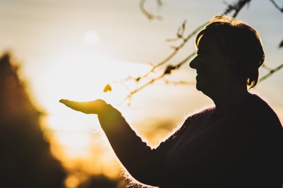 Eine Silhouette einer Frau, die mit der Hand die untergehende Sonne hält.